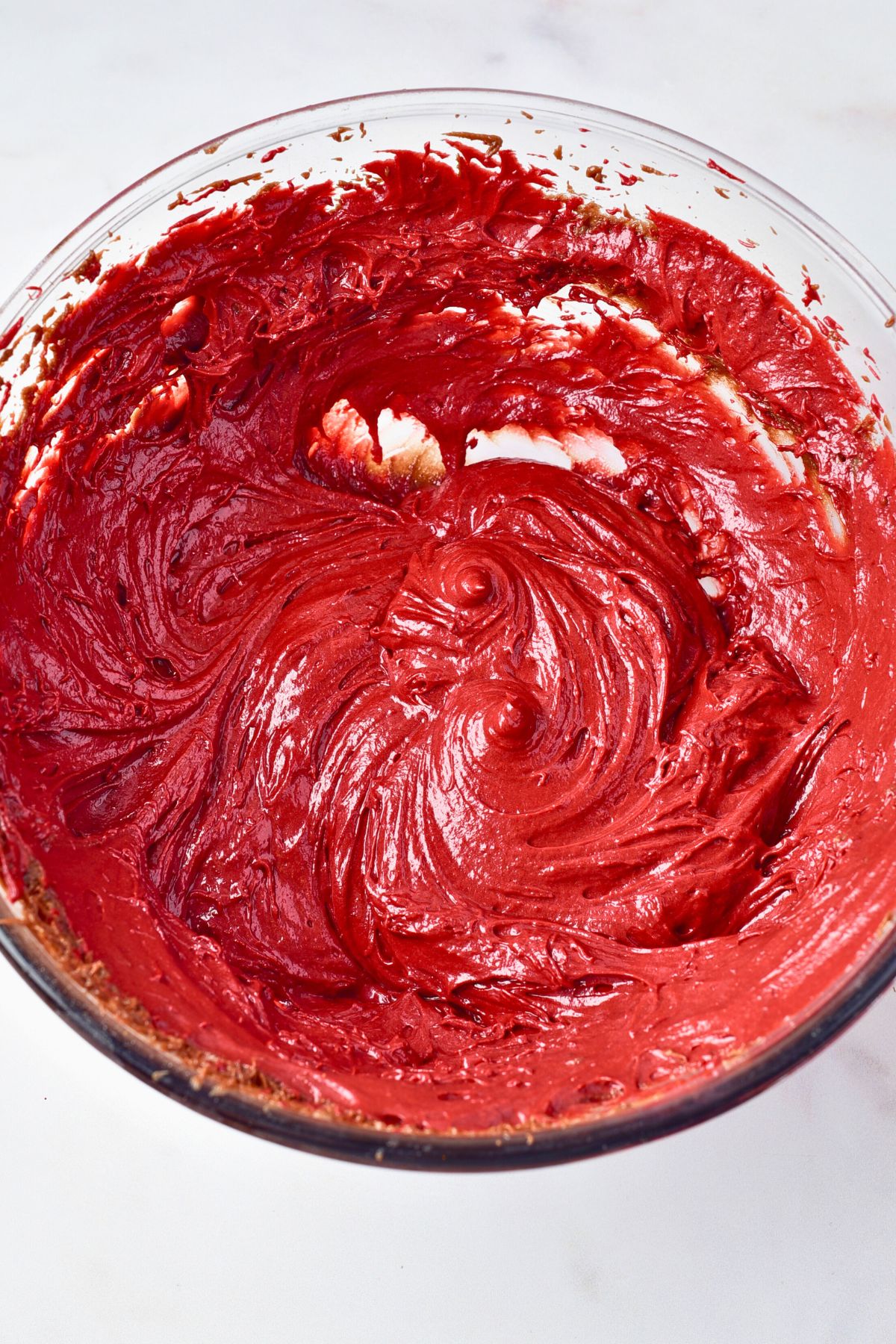 Bright red brownie batter in a clear glass bowl. 