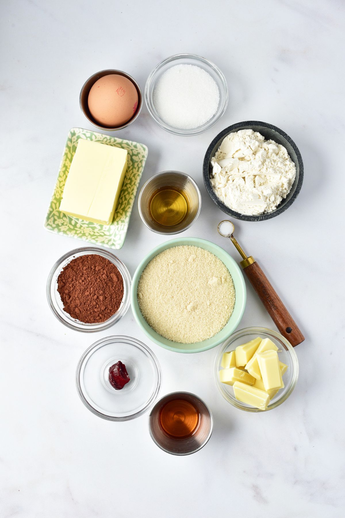 Ingredients needed to make red velvet brownies measured in small bowls on a white marble table. 