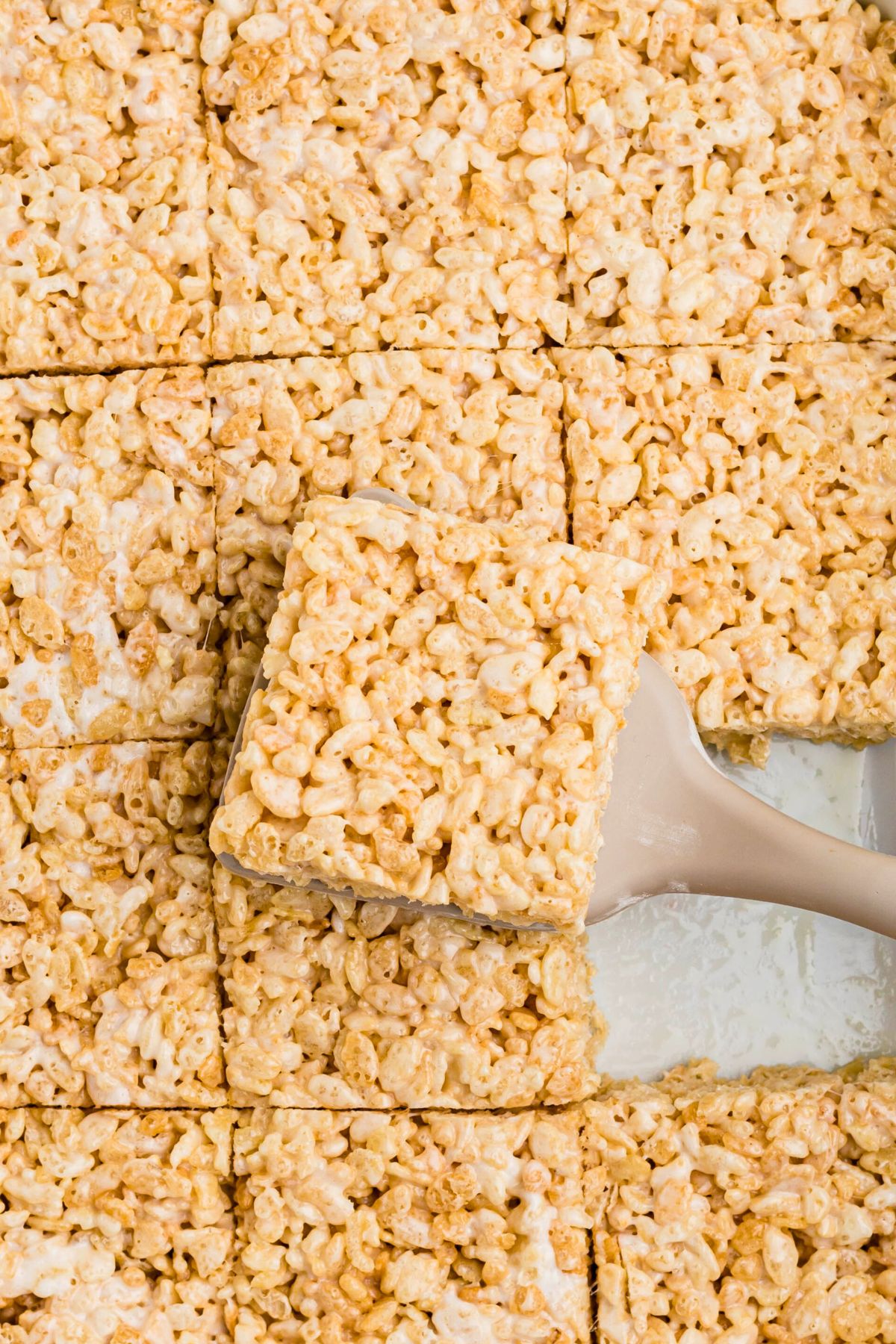 Rice krispie treats cut into squares with one piece being lifted out with a spatula. 