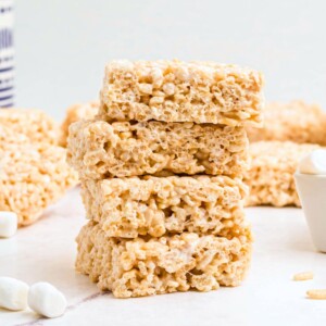 Four rice krispie treats stacked together on a white marble table with mini marshmallows on the table.