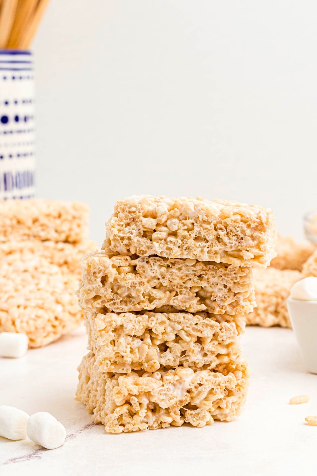 Rice krispie treats stacked on a marble table in front of other slices. 