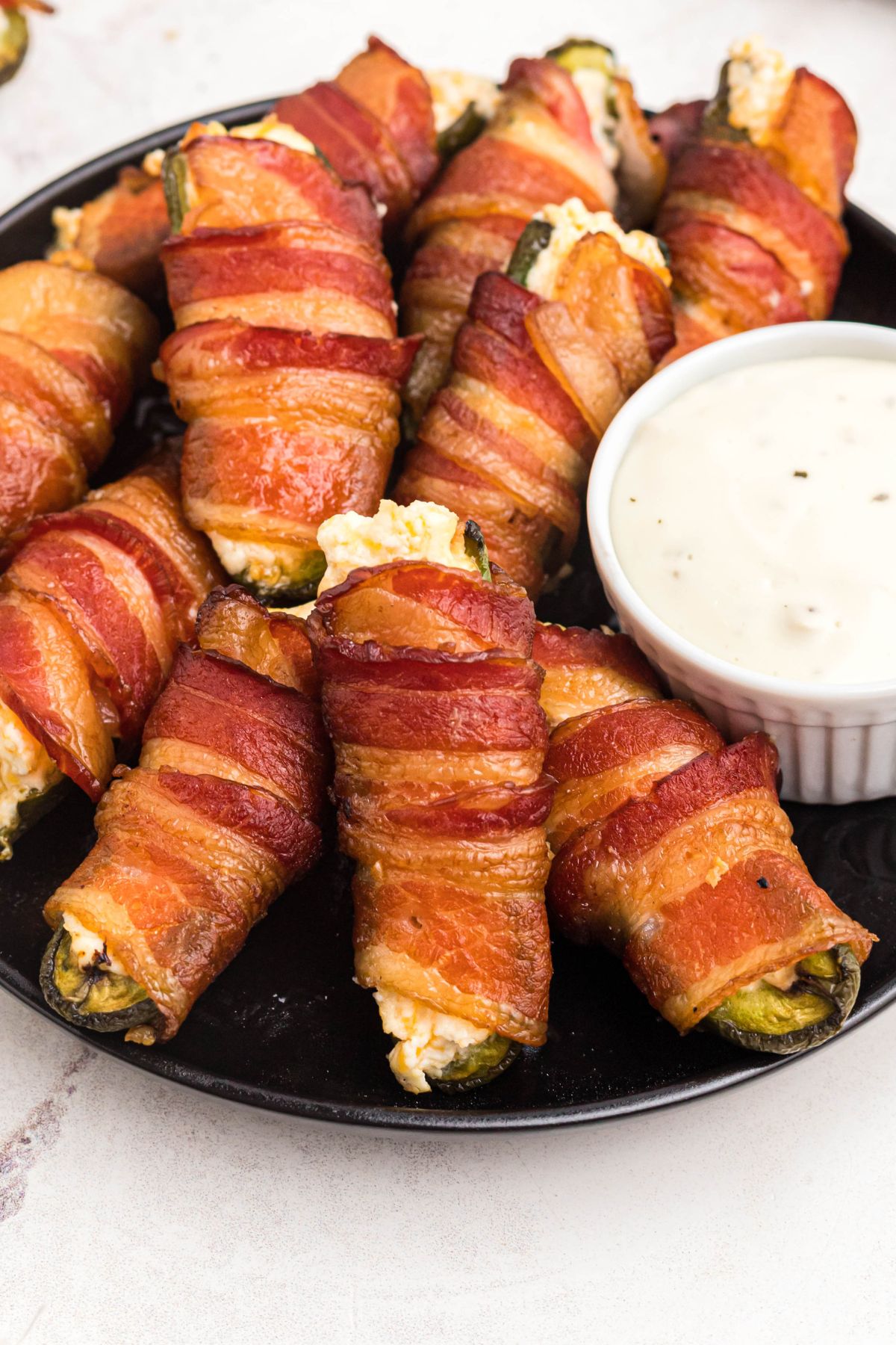 Smoked bacon wrapped jalapeno poppers stacked on a black plate.