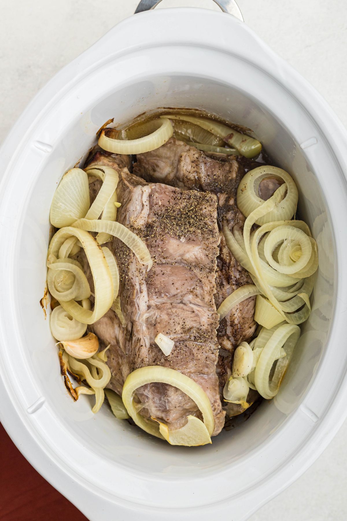 Baby back ribs in a white slow cooker after being cooked. 