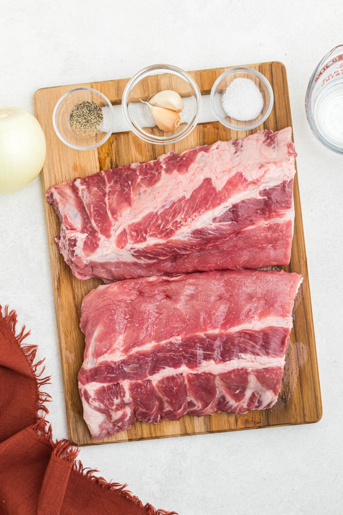 Uncooked ribs on a cutting board with seasonings in small bowls. 