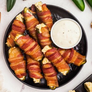 Smoked bacon wrapped jalapeno poppers stacked on a black plate.