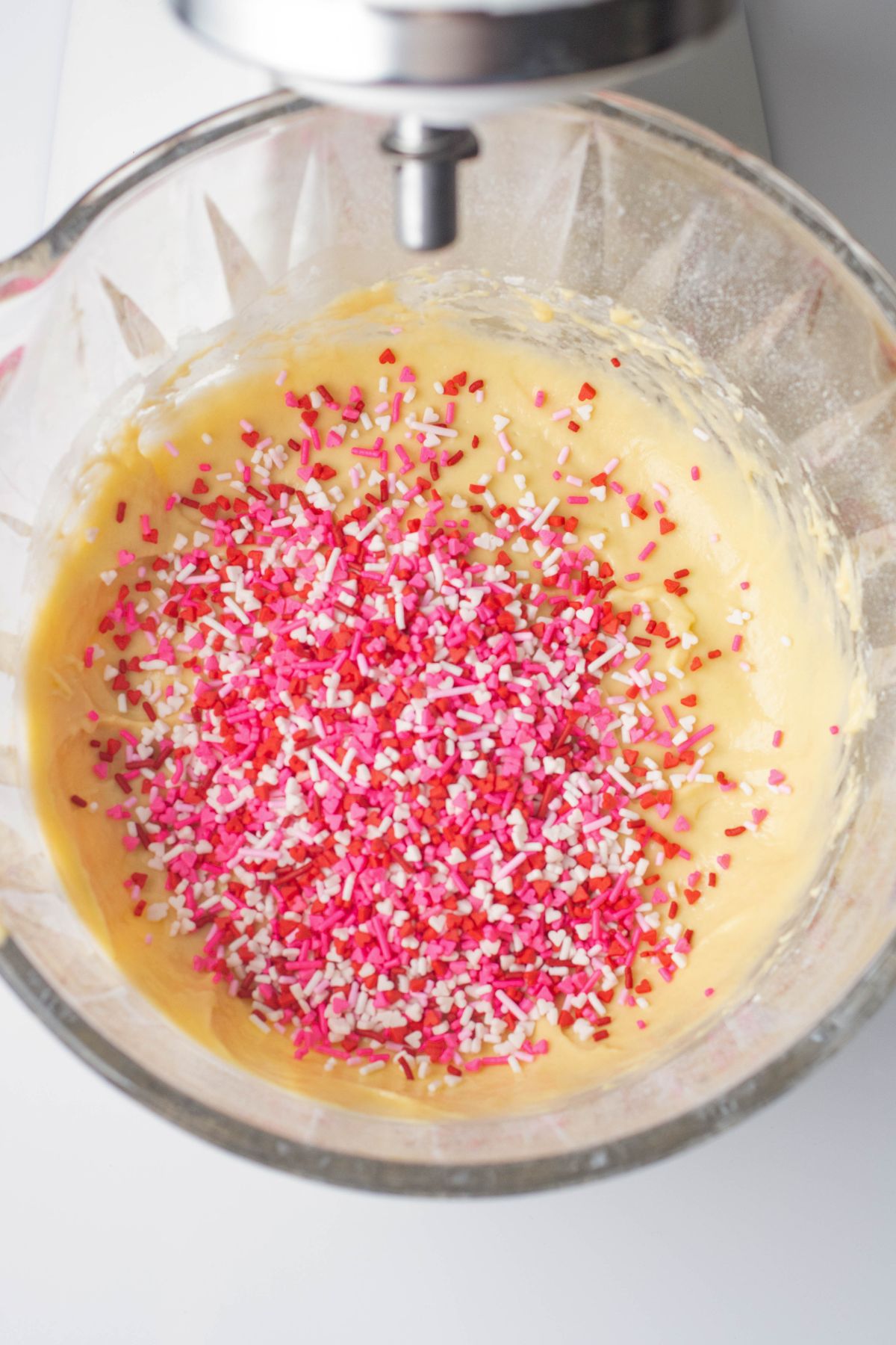 Valentine's Day sprinkles being mixed into pancake batter in a clear glass bowl. 