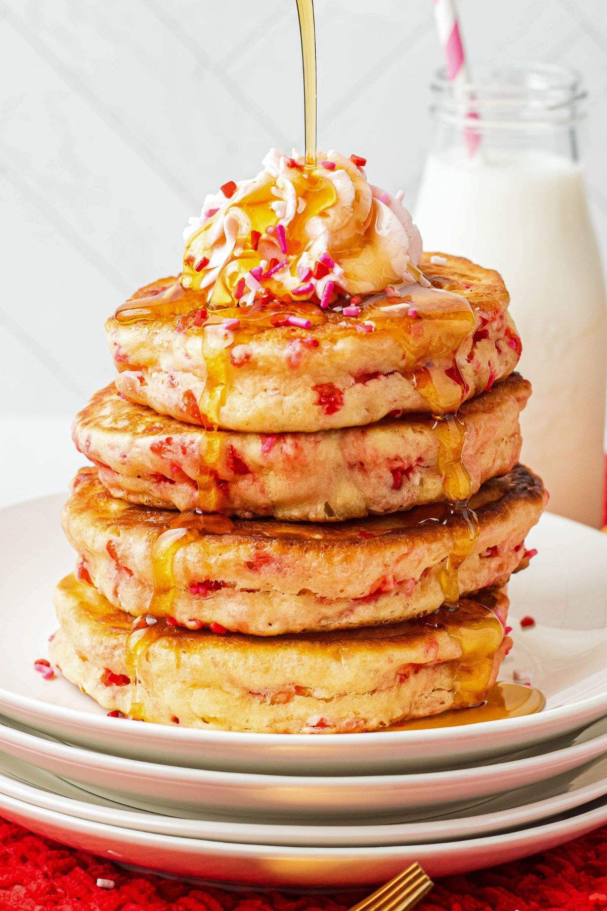 Golden fluffy Valentine's day pancakes stacked on a white plate with syrup being poured on top. 