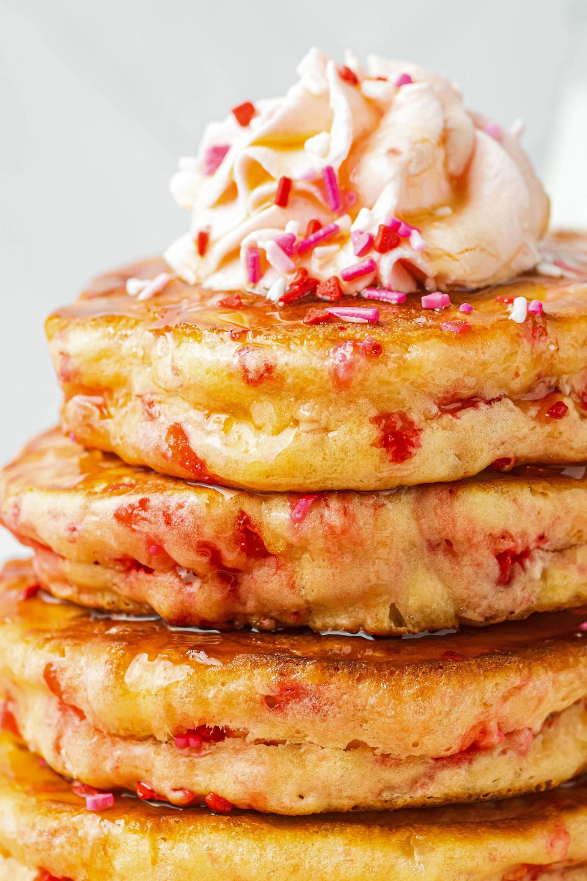 Close up image of pancakes stacked on a plate and topped with whipped cream and sprinkles. 