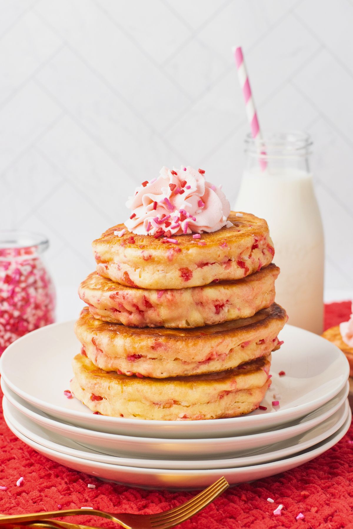 Light and fluffy golden pancakes with Valentine's sprinkles, stacked on a white plate. 