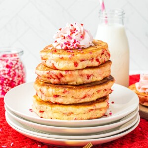 Golden fluffy stacked pancakes on a white plate, filled with Valentine's sprinkles.