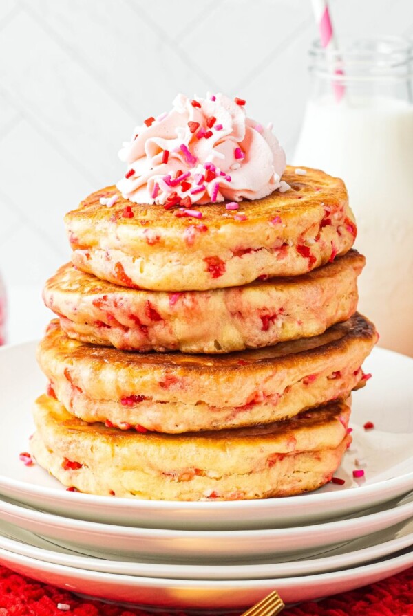 Golden fluffy stacked pancakes on a white plate, filled with Valentine's sprinkles.