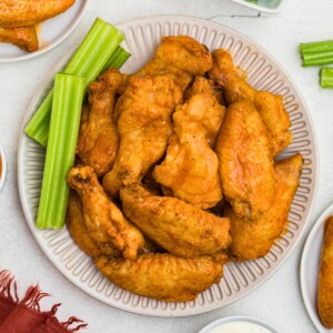 Crispy baked chicken wings, tossed in buffalo sauce, on a white plate with celery sticks on the plate.