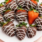 Chocolate covered strawberries on a white plate sitting on a pink table.