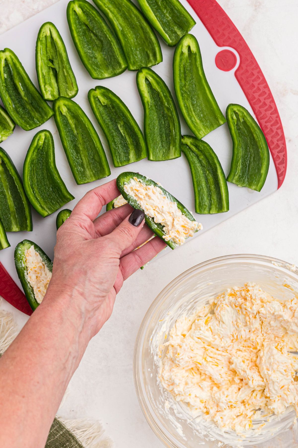 jalapeno peppers, cut in halves, being filled with cheese and cream cheese mixture. 