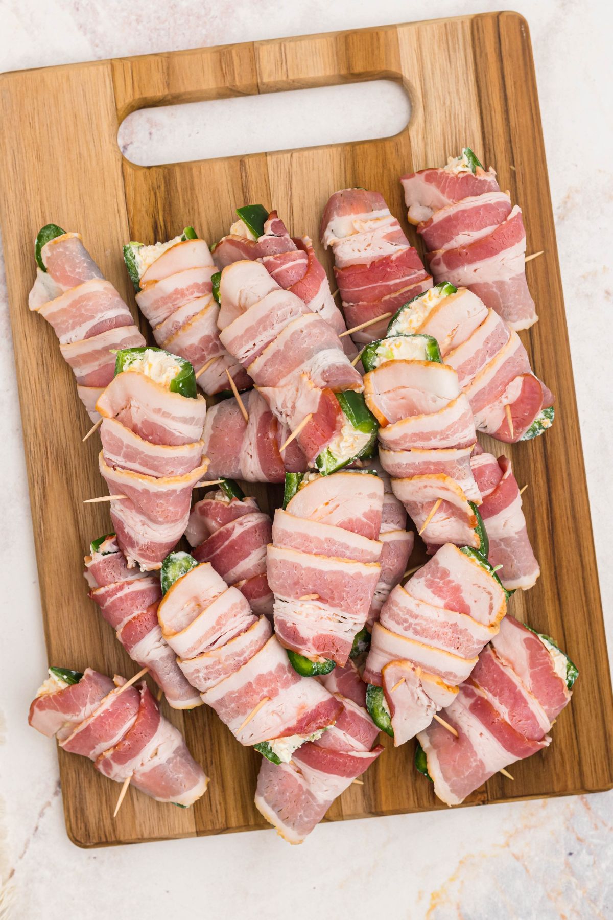 cutting board with bacon wrapped cheese stuffed jalapenos on top before baking.