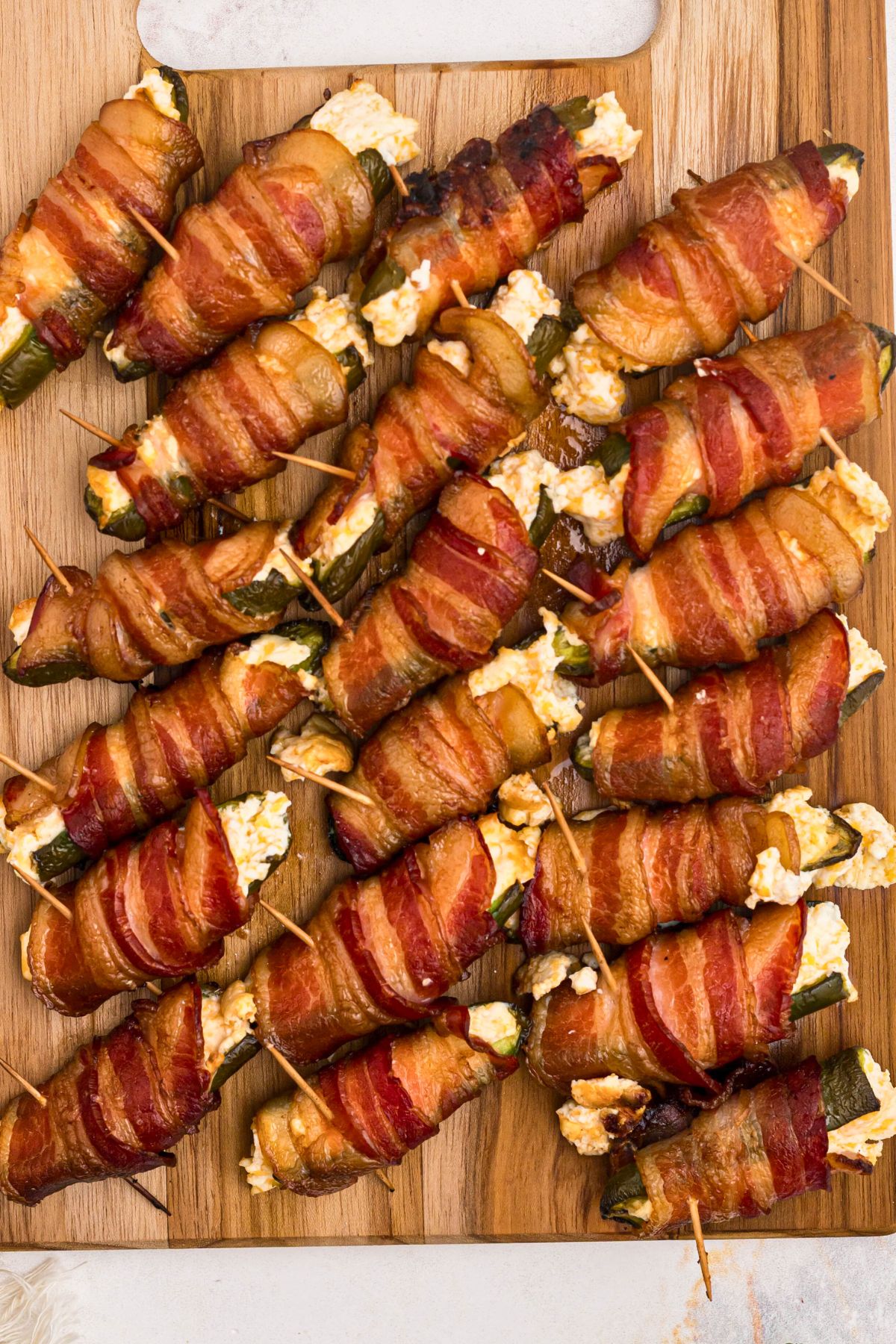 Golden crispy, bacon wrapped jalapeno poppers on a wooden cutting board after being smoked. 