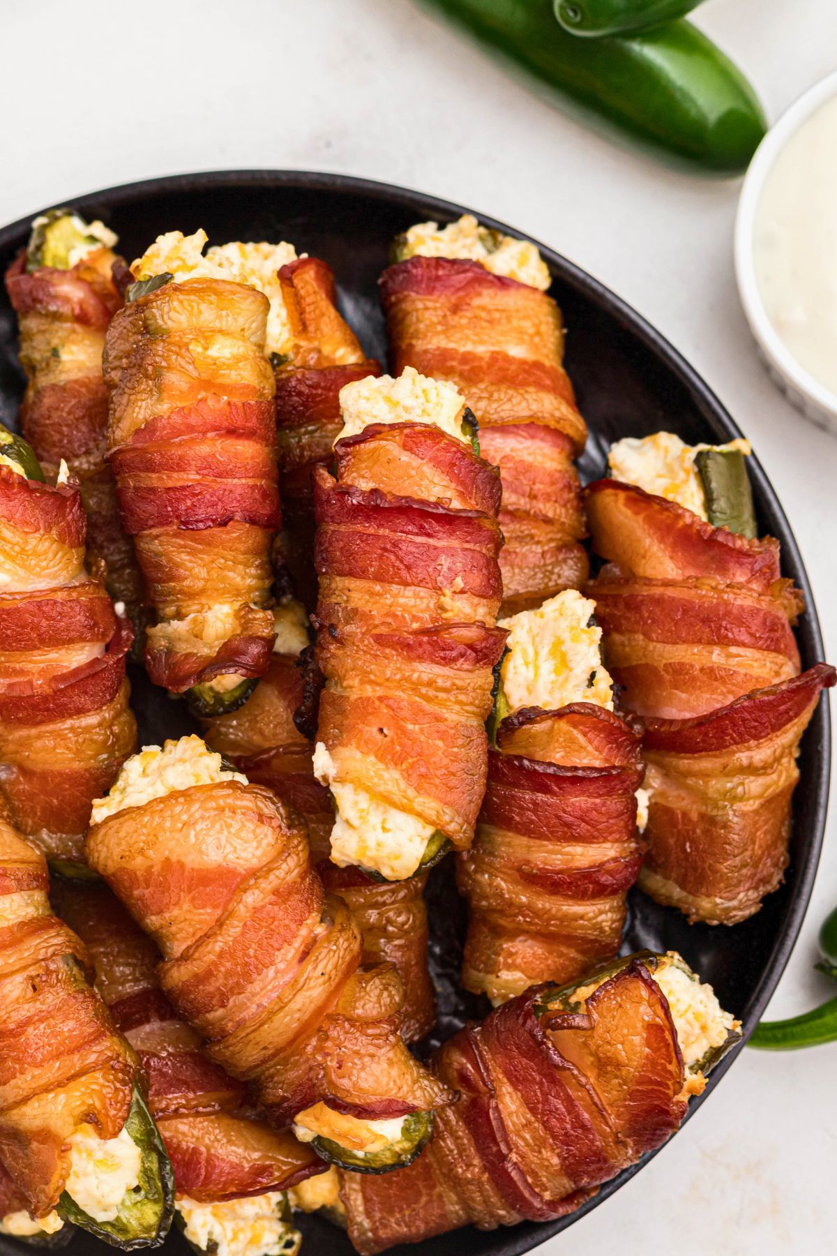 Golden bacon wrapped jalapenos stuffed with cheese stacked on a black plate. 