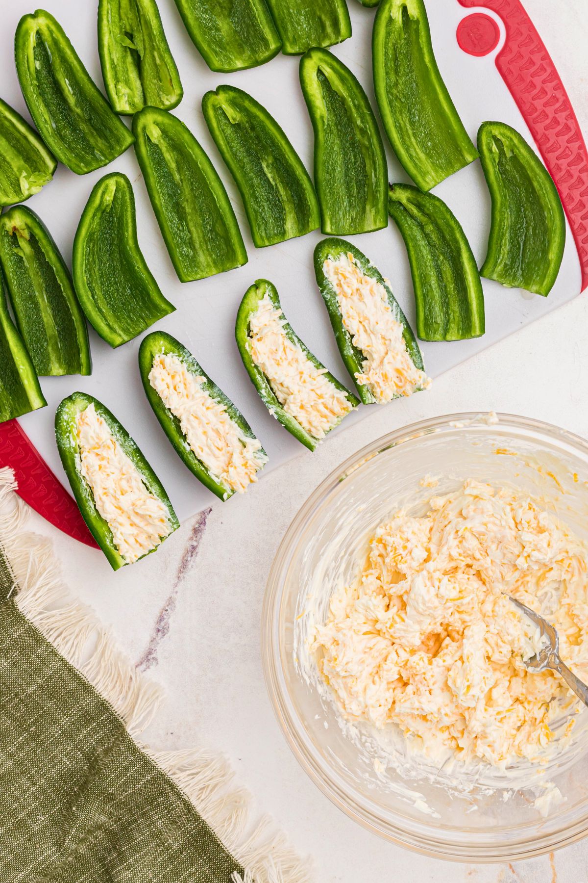 jalapeno peppers, cut in halves, being filled with cheese and cream cheese mixture.