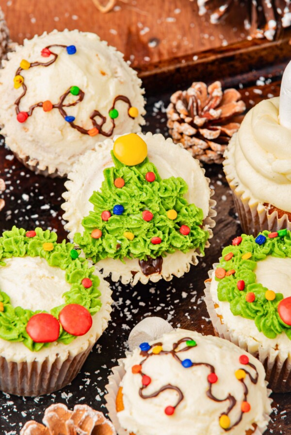 Christmas cupcakes with trees, wreaths, and lights decorations, on a table.