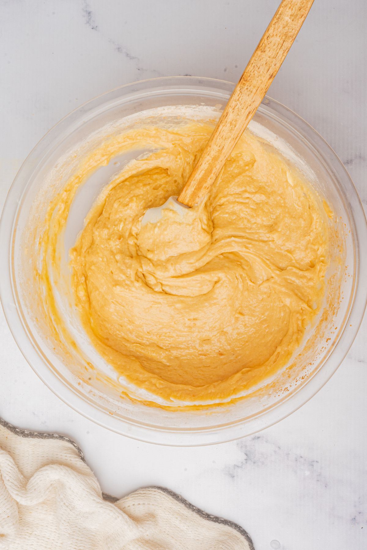 Cupcake batter mixed together a large glass bowl with a large wooden spoon. 