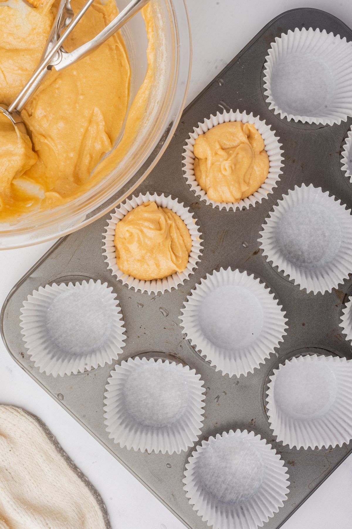 Cupcake liners being filled with cake batter using a portion scoop. 