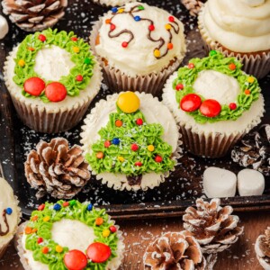 Christmas cupcakes with trees, wreaths, and lights decorations, on a table.