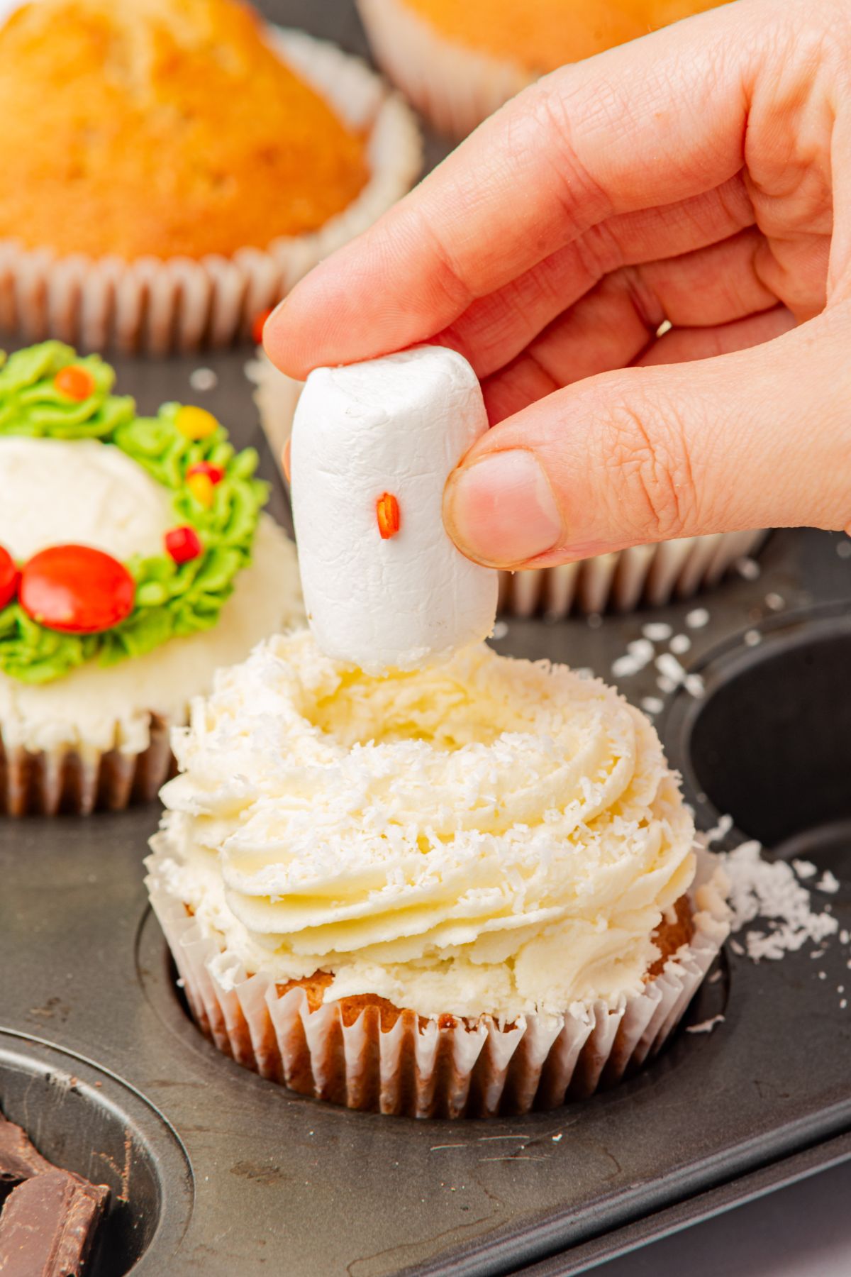 Snowman cupcakes being decorated with small marshmallows. 