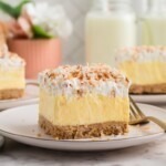 Slice of coconut delight on a small white plate with a fork on the side.