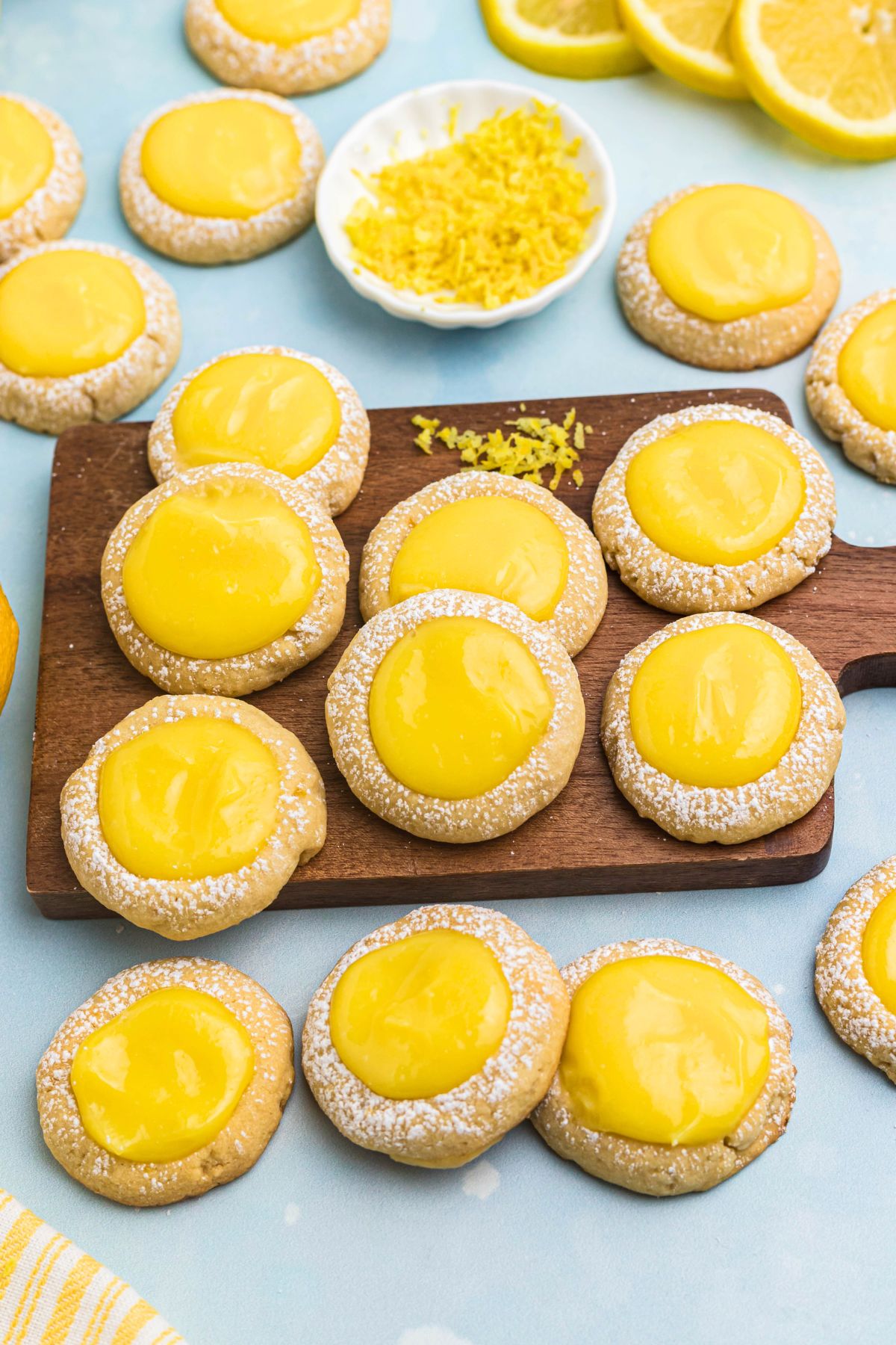 Lemon curd cookies on a small wooden board with lemon zest on the table in a small white bowl. 