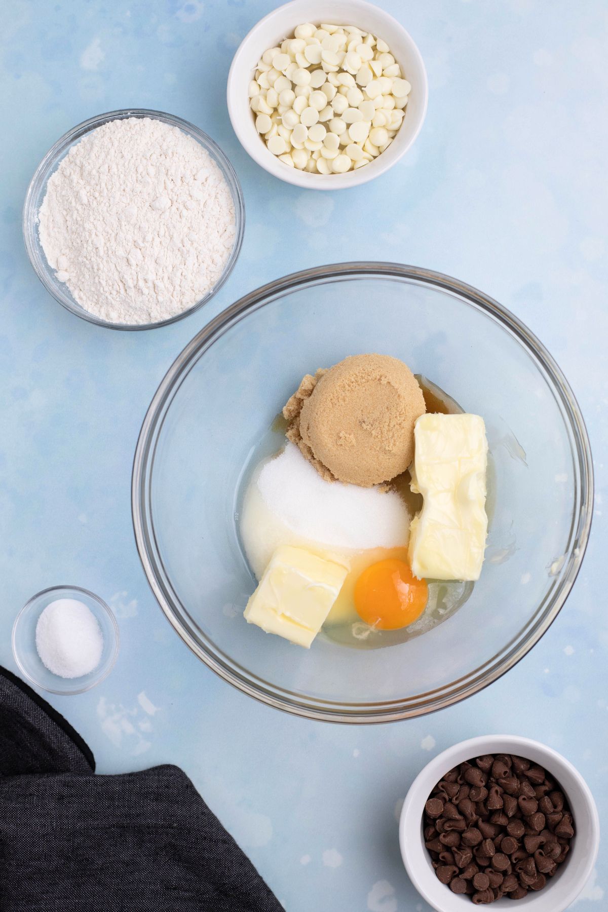 Butter and sugars in a clear glass bowl on a blue table.