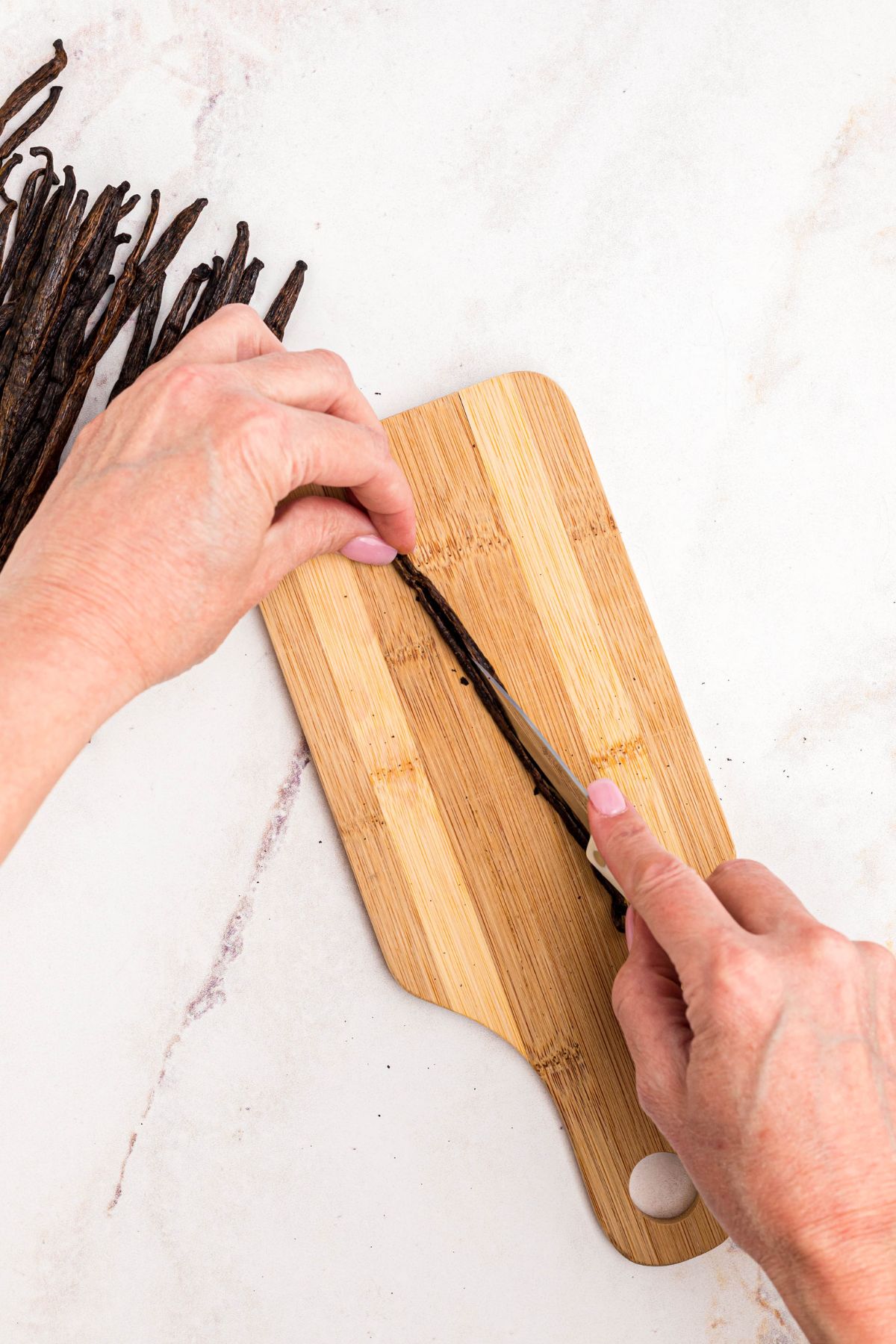 Cutting vanilla pods in the middle so seeds are exposed. 