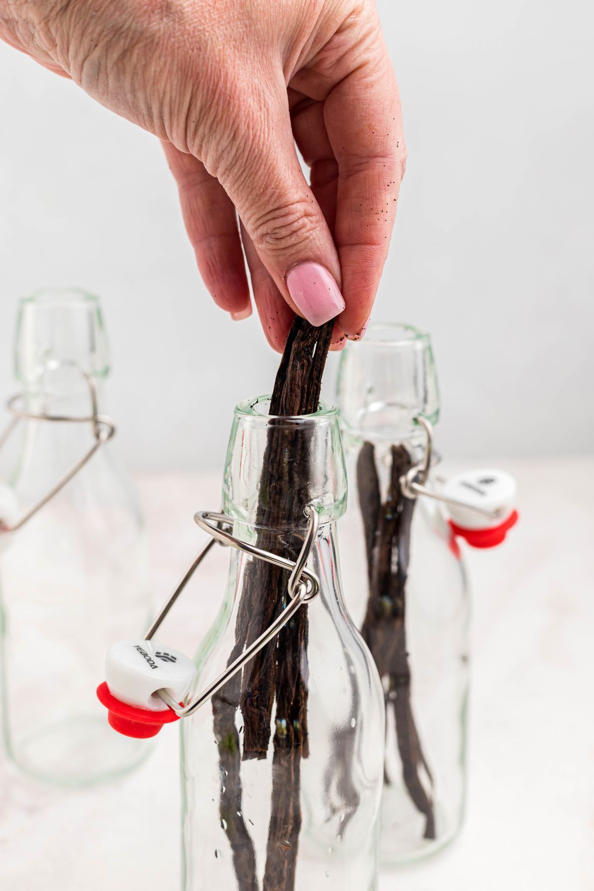 Vanilla pods being added into small bottles, after being sliced to reveal seeds to make homemade vanilla extract. 