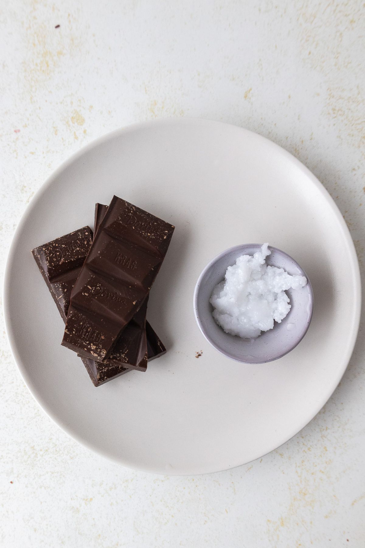 Chocolate and coconut oil on a small white plate before being combined to make chocolate curls.