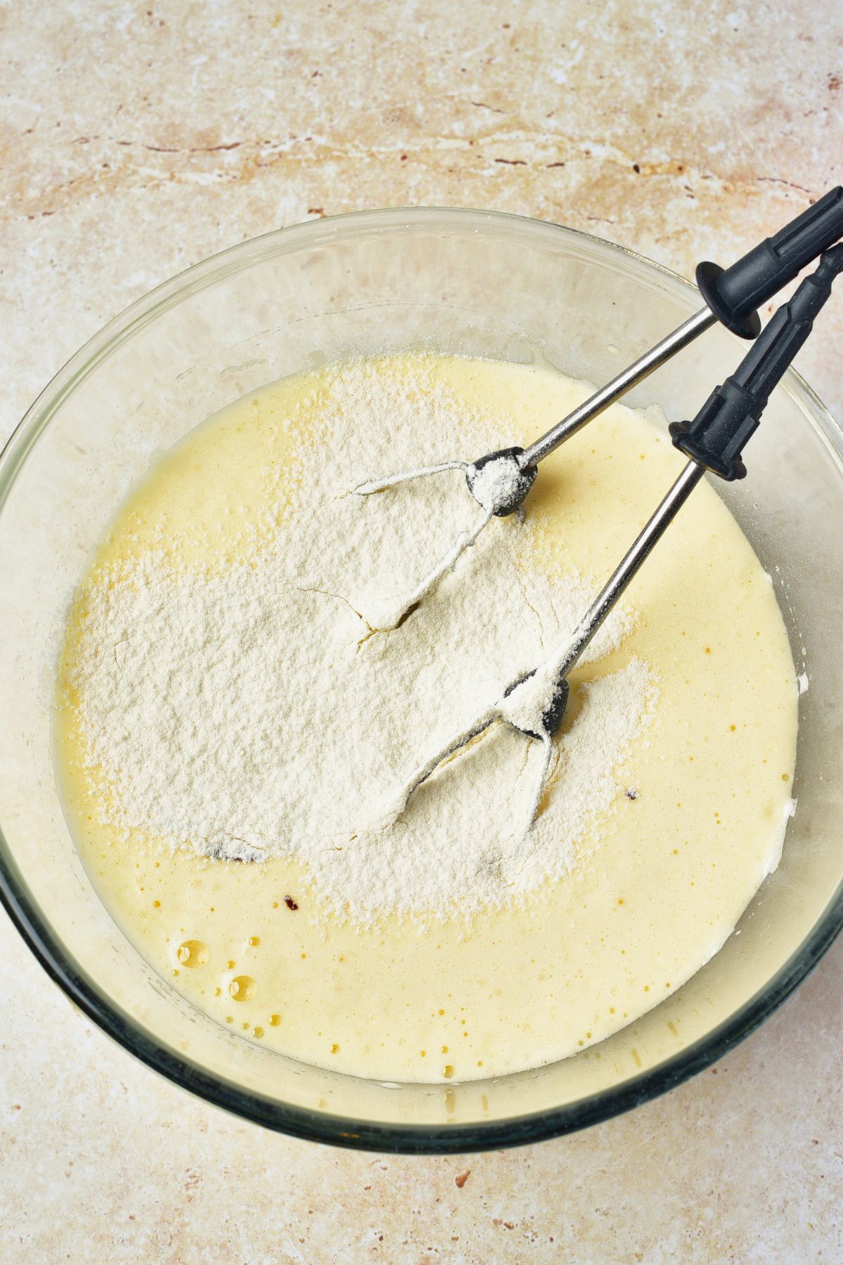 Creamy batter being mixed together in a large glass bowl. 