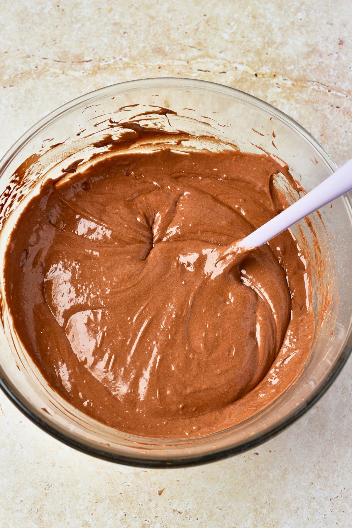 Creamy chocolate batter mixed together in a clear mixing bowl. 