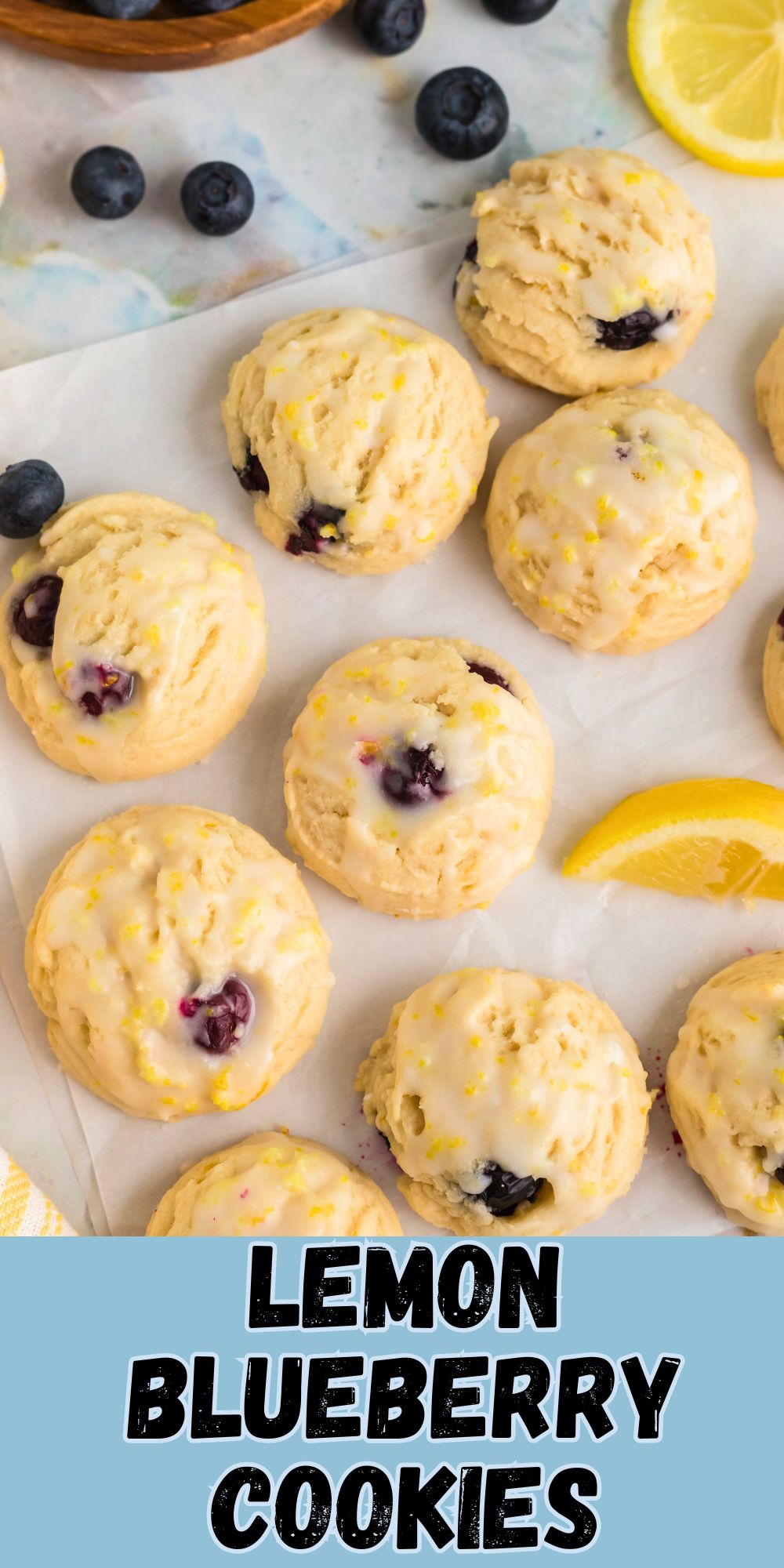 Lemon blueberry cookies on parchment paper with lemon wedges and blueberries scattered next to them.