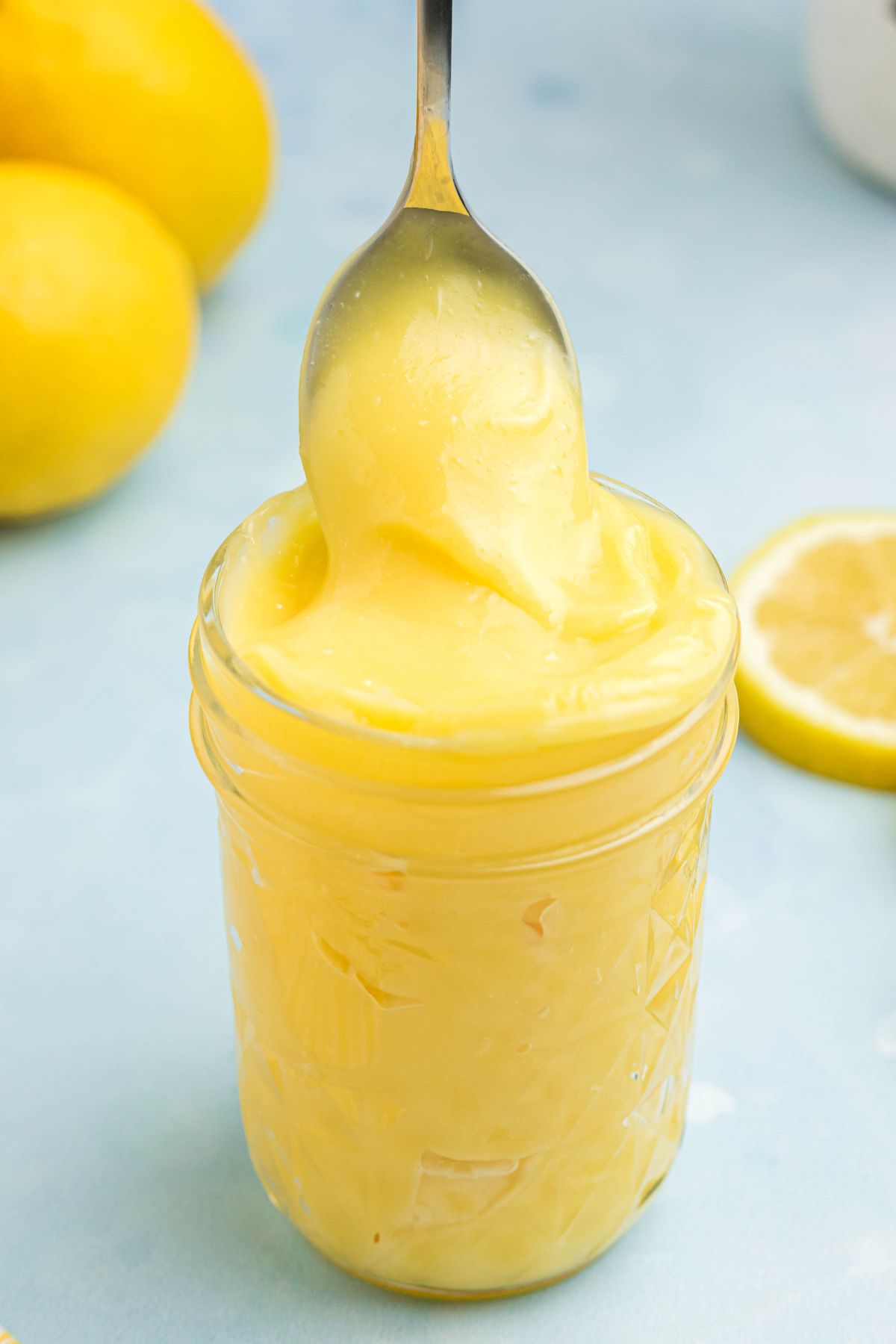 Bright yellow lemon curd in a small jar with a spoon being scooped out. 