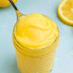 Bright yellow lemon curd in a small jar with a spoon being scooped out.