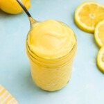 Bright yellow lemon curd in a small jar with a spoon being scooped out.