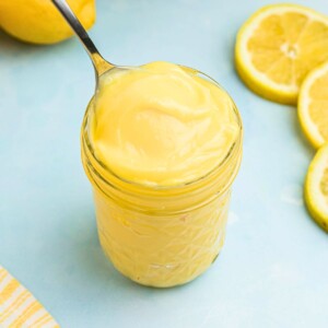 Bright yellow lemon curd in a small jar with a spoon being scooped out.