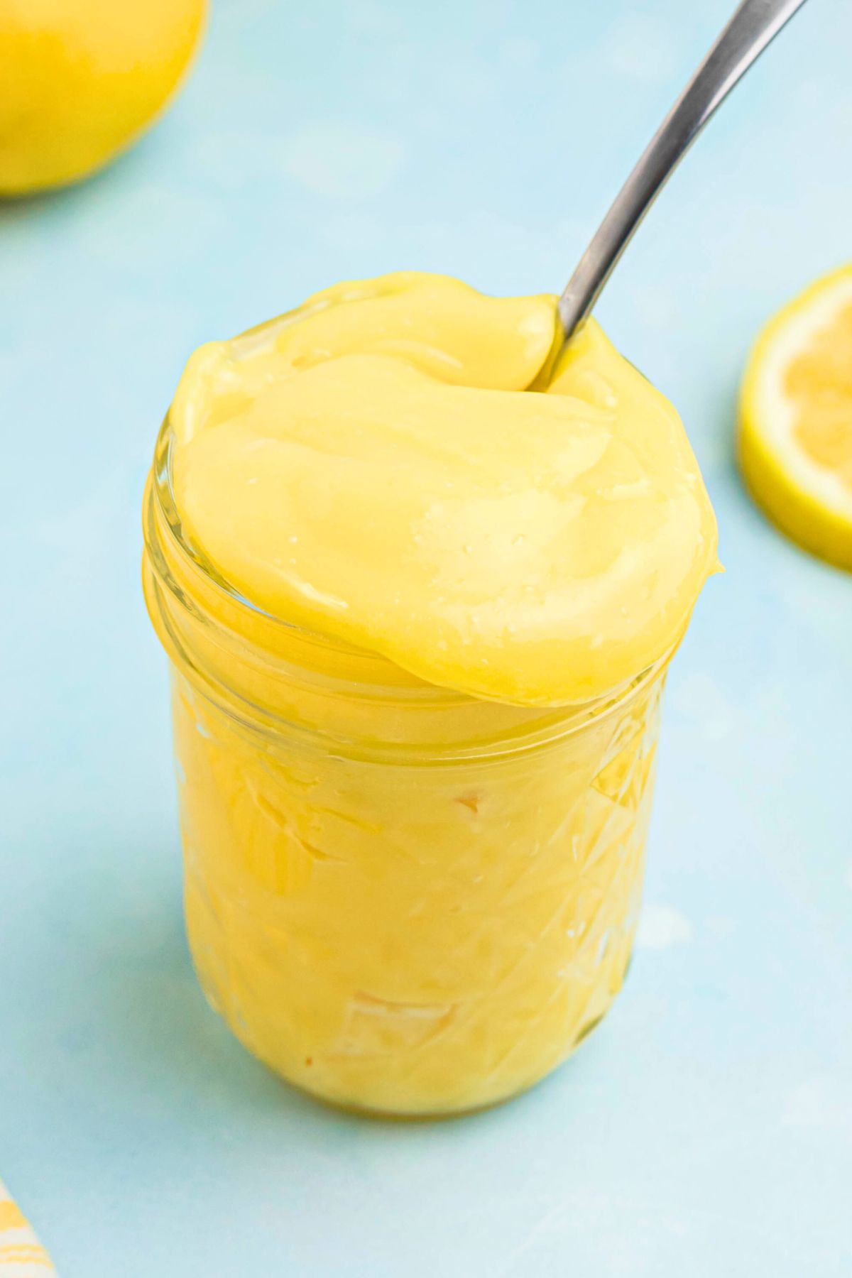 Bright yellow lemon curd in a small jar with a spoon being scooped out.