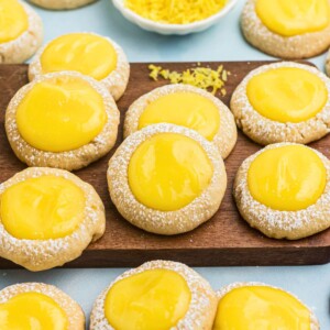 Shortbread cookies topped with a spoonful of lemon curd on a small wooden cutting board.