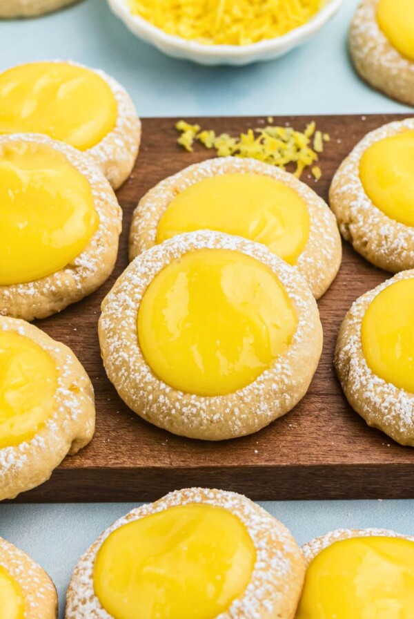 Shortbread cookies topped with a spoonful of lemon curd on a small wooden cutting board.