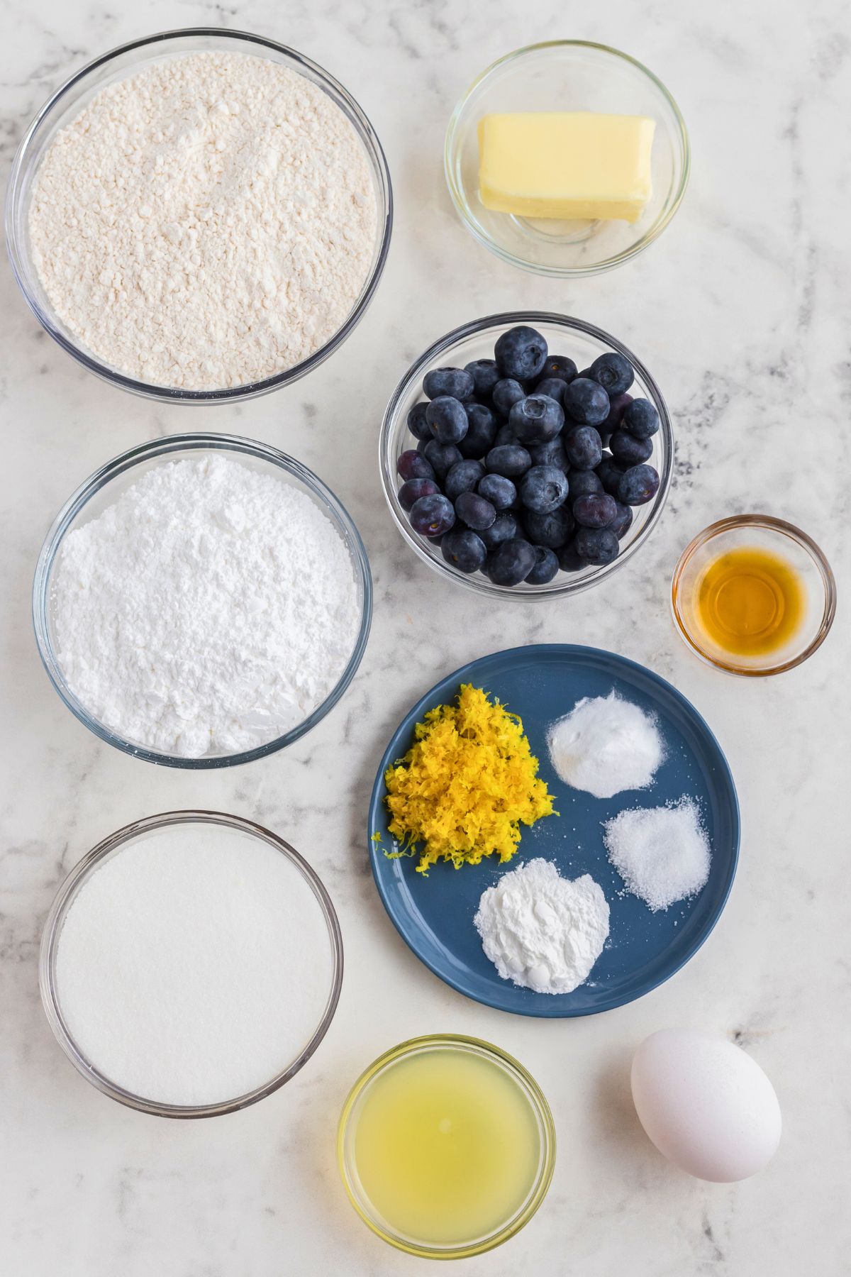 Ingredients needed to make cookies measured out into small bowls and dishes, on a marble table. 