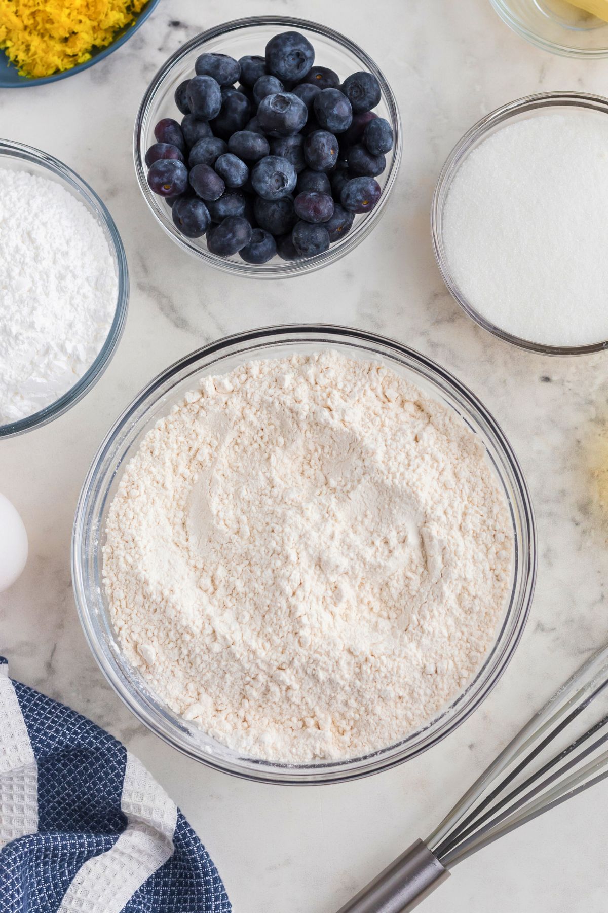 Dry ingredients being mixed together in glass bowls on a marble table. 