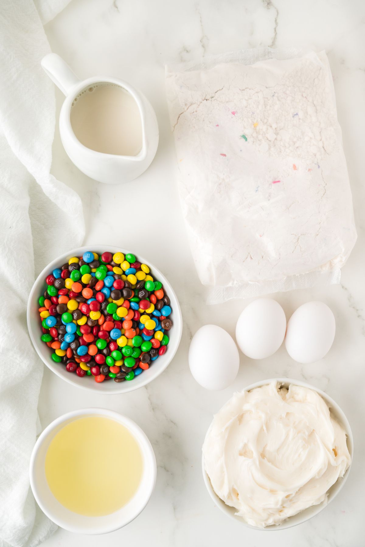 Ingredients needed to make cupcakes with mini m and m's measured into small white bowls. 
