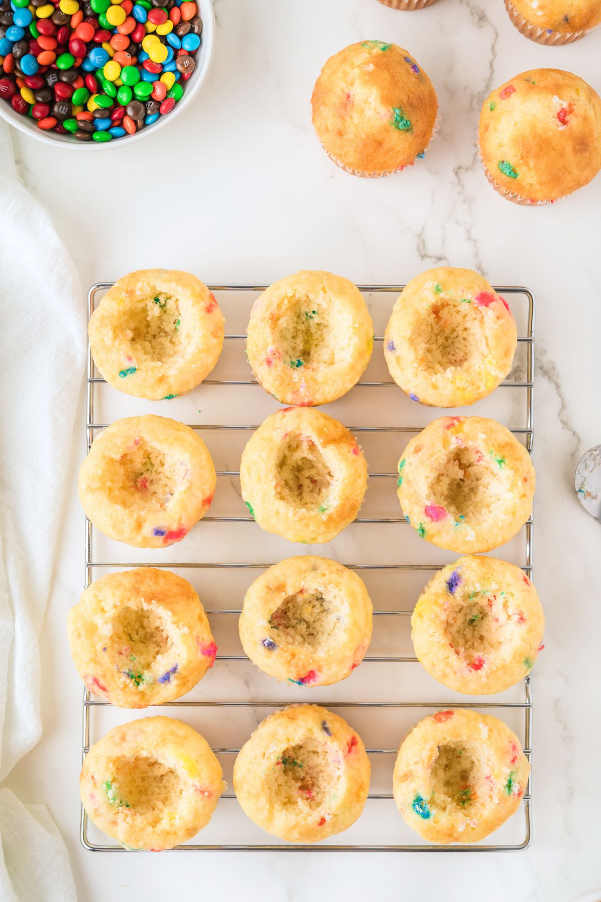 Funfetti cupcakes on a cooling rack, with the center scooped out. 