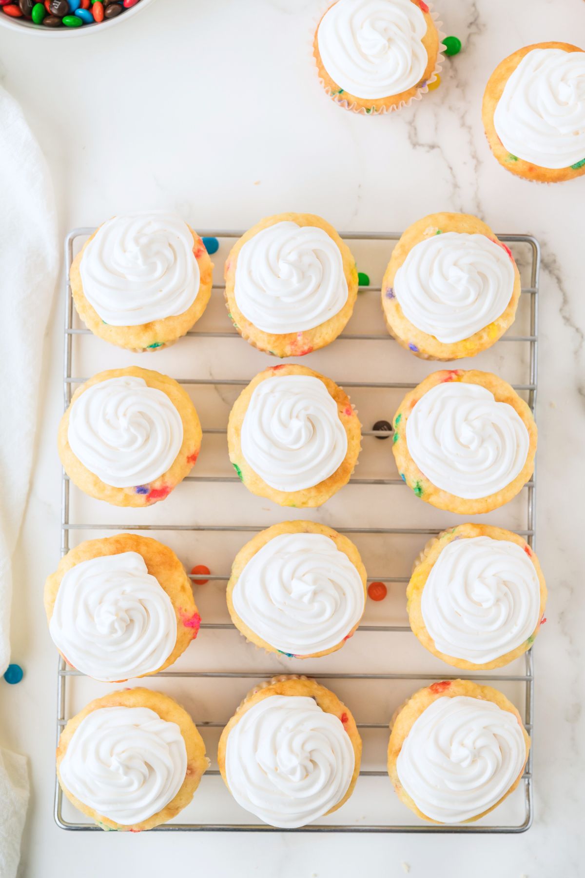 Cupcakes on a cooling rack, frosted with vanilla frosting. 