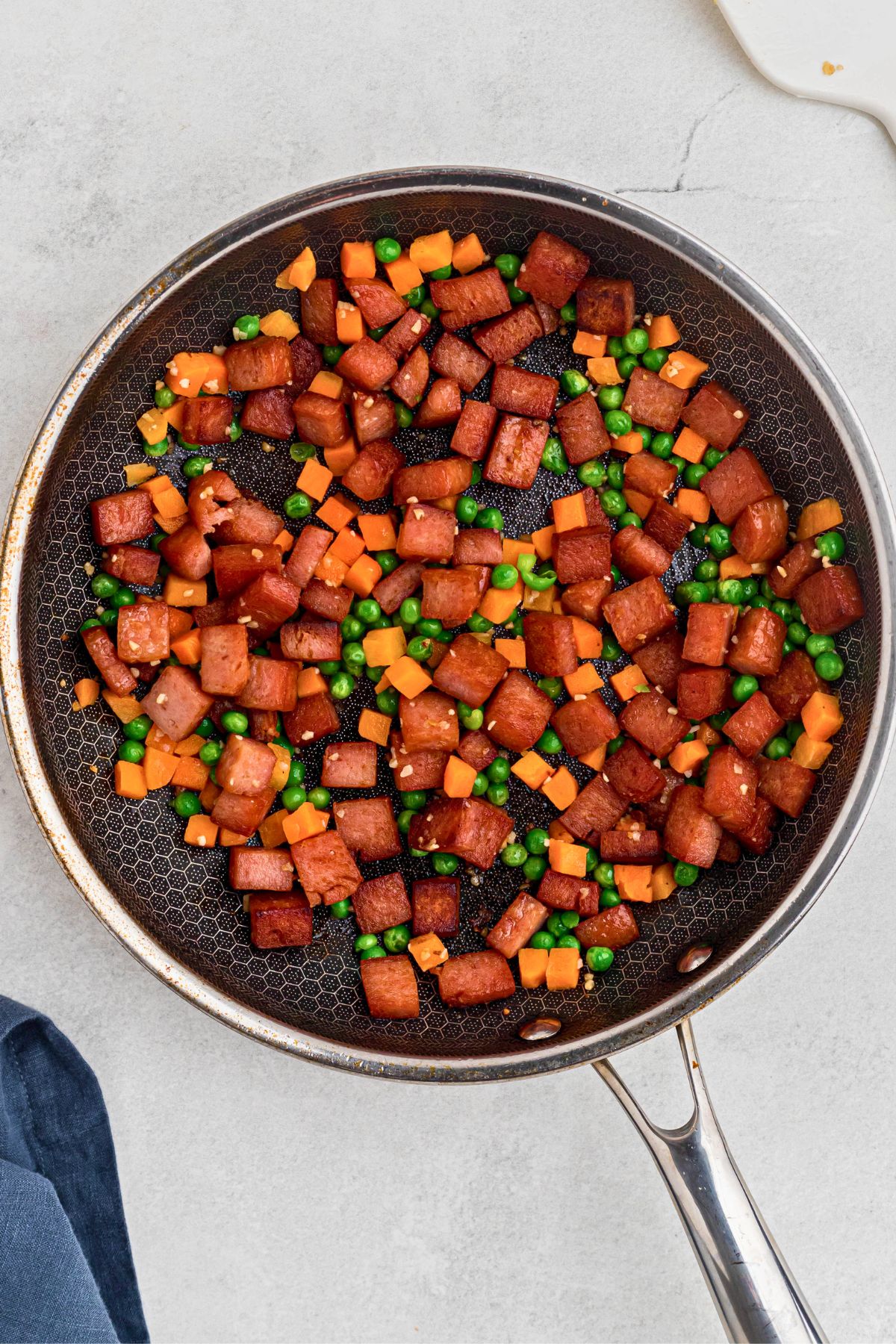 Spam, veggies, and other ingredients being cooked together in a skillet. 