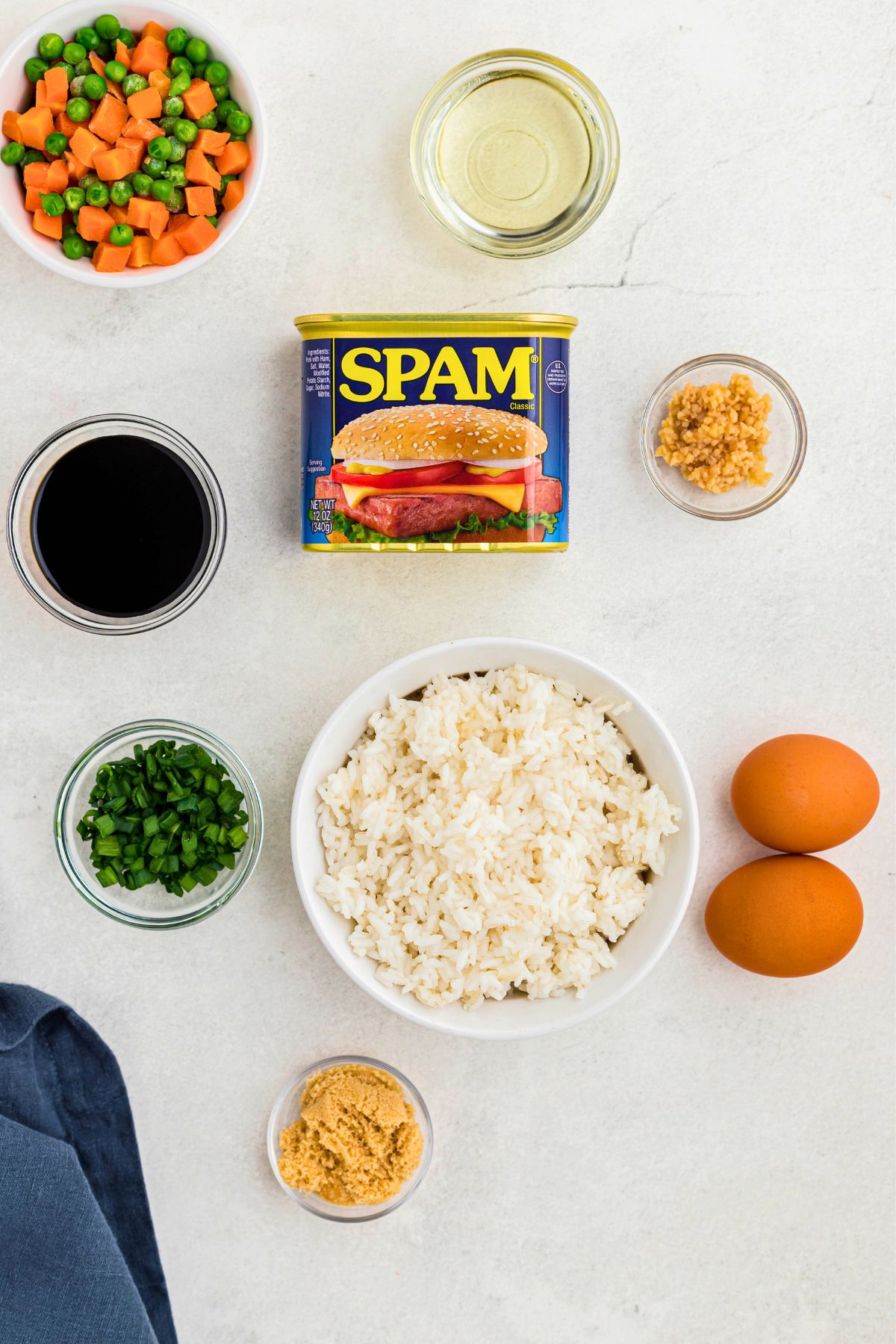 Ingredients needed to make spam fried rice measured out in small bowls on a white marble table. 